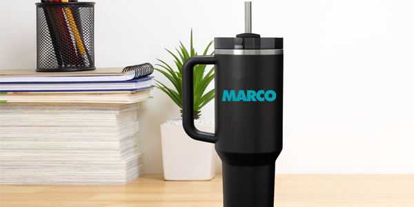 Black insulated tumbler with a handle and the MARCO logo sitting on a desk next to office supplies.